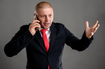 Businessman dressed in black suit talking on the phone he starts to gesticulate with his hand...