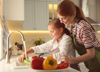 Mother and daughter washing vegetables in kitchen