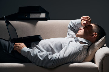 Fototapeta premium businessman is lying on the sofa with laptop and resting