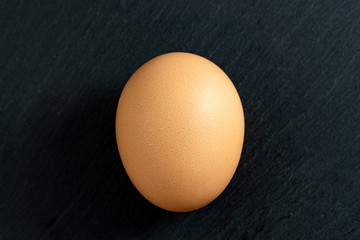 One brown chicken eggs black background, close up, top view