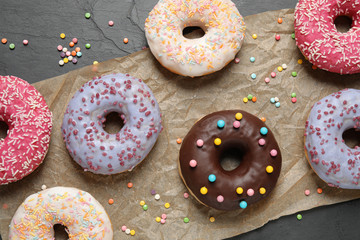 Yummy donuts with sprinkles on dark background, flat lay