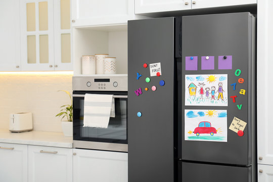 Modern refrigerator with child's drawings, notes and magnets in kitchen. Space for text
