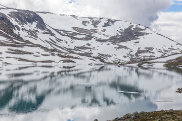 Fototapeta na wymiar snow mountains surrounded by clouds in norwegian fiord reflection in water, selective focus