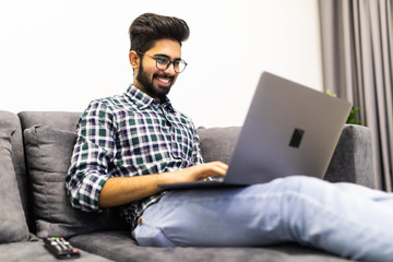 Indian bearded man relaxing on sofa with laptop at home