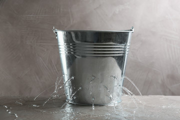 Leaky bucket with water on table against grey background - obrazy, fototapety, plakaty
