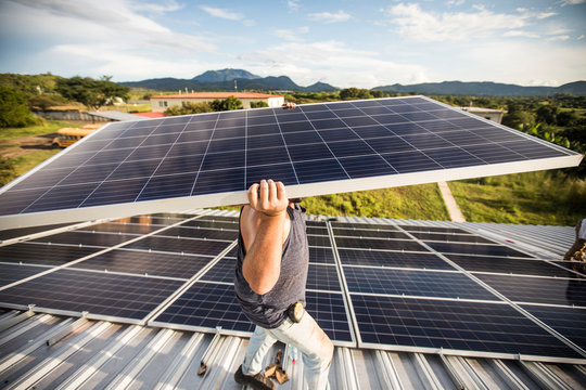 strong construction worker carries solar panel above head on roof. - Powered by Adobe