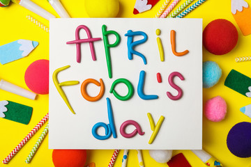 Paper note with phrase APRIL FOOL'S DAY and decor on yellow background, flat lay