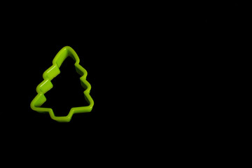 Green plastic cookie cutter for making cookies in the form of a Christmas tree on a black...