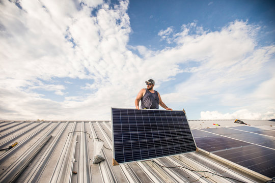 Low angle of construction worker installing solar panels on roof.