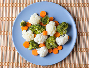 Vegetables on a grey plate over a wood mat. Broccoli, cauliflower and carrot cooked. Healthy vegan food.