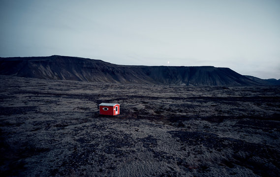 Small Red House In Dark Dry Terrain Surrounded By Hills