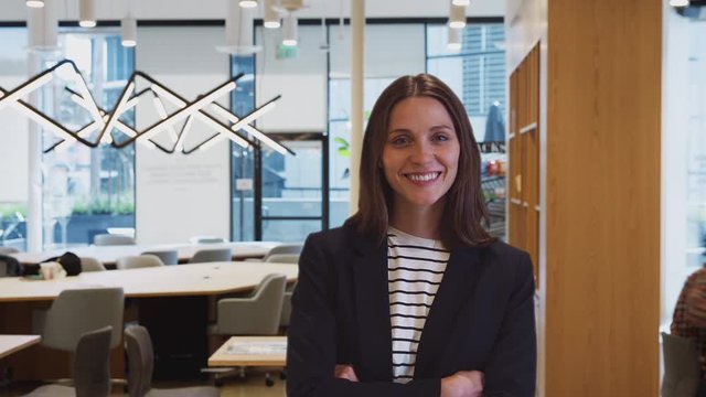 Businesswoman standing in busy modern open plan office with time lapse of busy colleagues in background