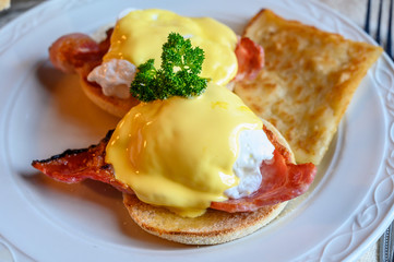 Weekend brunch in Scotland with two eggs benedict on homemade muffuns with roasted bacon and yellow hollandaise sauce.