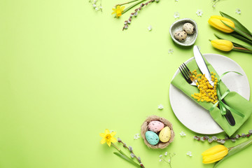 Festive Easter table setting with eggs and floral decor on green background, flat lay. Space for...