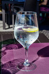 Drinking cold mineral water with bubbles, served in wine glass with ice cubes and lemon