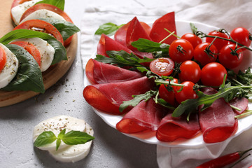 The concept of Italian cuisine. Italian dried ham from beef. Meat snack. Bresaola with arugula and tomatoes, mozzarella, basil and chili pepper. Caprese. Background image, copy space