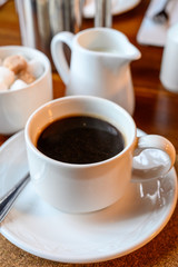 White cup with black coffee and  hot milk jug