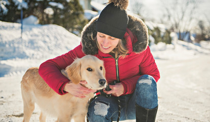 Attractive mid adult blond woman in snow with Golden Retriever.
