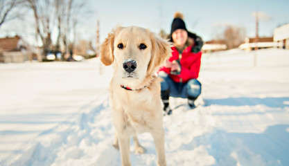 Attractive mid adult blond woman in snow with Golden Retriever.