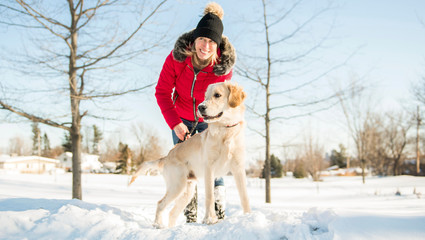 Attractive mid adult blond woman in snow with Golden Retriever.