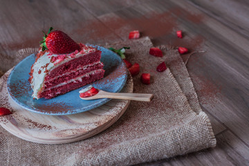 Red Velvet cake on a blue plate with strawberries and pure cocoa with a rustic background with flowers and cloth napkins