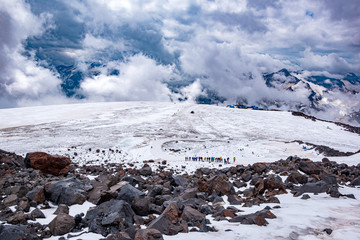 Landscape view of glacier and alpinists climbing by the path. Mount Elbrus, Caucasus, Russia.  Clouds and mountains in the background.