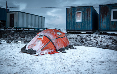 Close up of expedition tent, secured with rocks, covered with snow. Mount Elbrus, Caucasus, Russia.  Accommodation in mountains.  Front View. Metal conteiners in the Background.