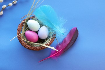 Happy Easter, decor, basket with painted eggs, bright feathers on a blue background