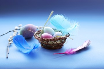 Happy Easter, decor, basket with painted eggs, bright feathers on a blue background