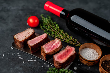 slices of different roasts of steaks on a knife and a bottle of wine on a stone background