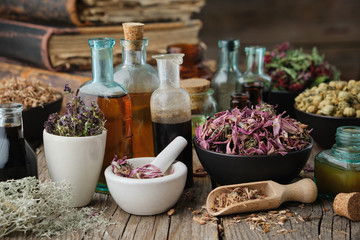 Bottles of healthy tincture or infusion, mortar and bowls of medicinal herbs, old books on table....
