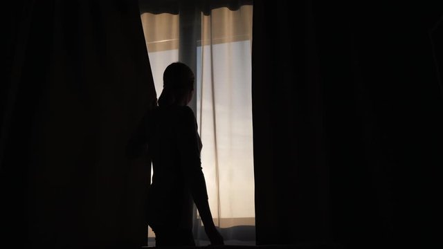 The silhouette of a woman, closes the curtain on the window