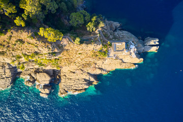 Top view on a lighthouse standing on the rocky hill near the sea with blue turquoise water in Portofino, Italy. Ligurian sea washes a coast with the big stones.