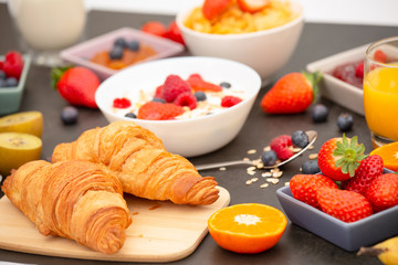 Breakfast Served in the morning with Butter croissant and corn flakes Whole grains and raisins with milk in cups and Strawberry, Blueberry, Raspberry, Kiwi, Fresh Orange Juice on the breakfast table.