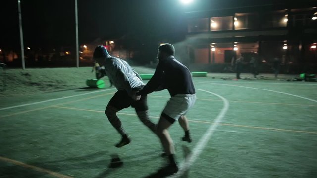 People having intense rugby training in pairs on the field at night