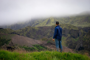 Fototapeta premium Backside of tall caucasian man wearing green jacket standing in over mountain and fog background. Promoting healthy lifestyle