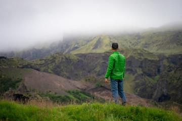 Fototapeta premium Backside of tall caucasian man wearing green jacket standing in over mountain and fog background. Promoting healthy lifestyle