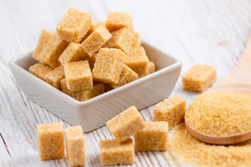 Brown sugar in a square cup and wooden spoon on a wooden table, healthy sugar is used for cooking food or desserts.