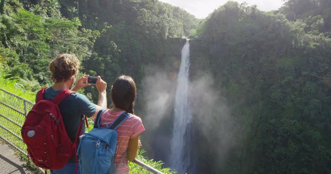 Tourist couple on Hawaii taking pictures of the famous Akaka Falls waterfall on Hawaii, Big Island, USA. Happy cheerful young multicultural couple tourists on travel.