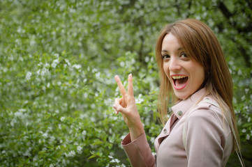 Blonde woman is showing victory on flowering tree background in the garden during early spring. Allergy concept