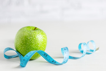 Green apple and tape measure around it on white wooden background.