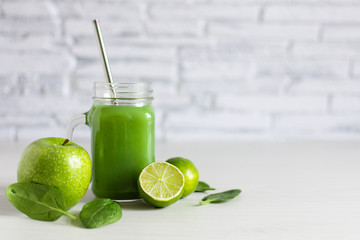 Mason jar of detox green smoothie made with apple, spinach and lime on white wooden table.