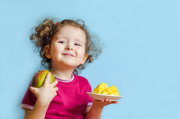 Beautiful curly happy girl with mango on blue background. human emotions from food