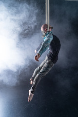 Circus artist on the aerial straps with costume on the black and smoked background.