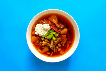 Borscht soup in a white bowl on blue background. Top view. Famous traditional Ukrainian and Russian borshch soup with beetroot and cabbage. Red Eastern Europe soup.
