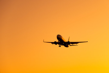 Large airliner passengers view is landing on the landing strip at the airport against the backdrop of bright orange sunset on a sunny summer day. A plane flies in the sky at sunset day