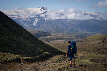 Backside of tall caucasian backpacker standing in over mountain and fog background on the Laugavegur hiking trail. Iceland