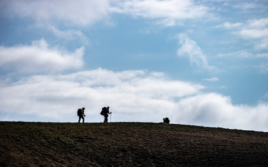 Silhouettes of people walking with backpacks on the sky background
