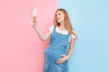 Happy beautiful young pregnant girl takes a selfie on her smartphone in the Studio