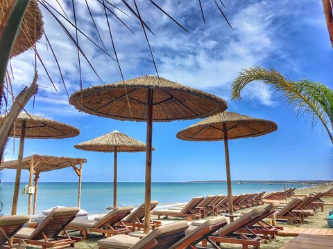 Sun loungers and straw umbrellas on the seashore on the beach of Cyprus on a sunny day. Beautiful beach background for summer travel with sun. beach vacation concept.cessed with Snapseed.